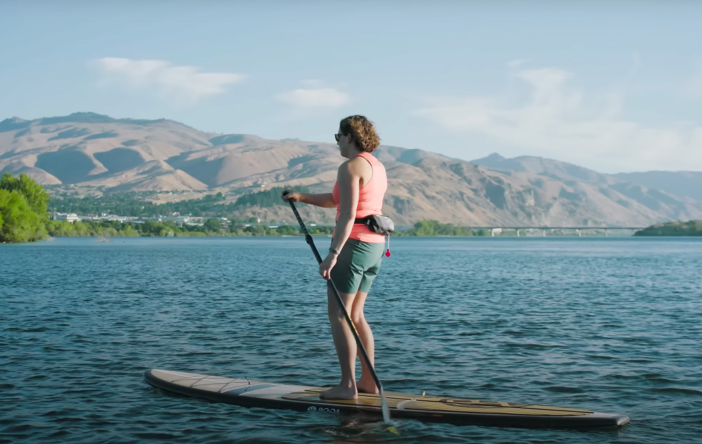 Woman paddleboarding on calm lake with mountains.