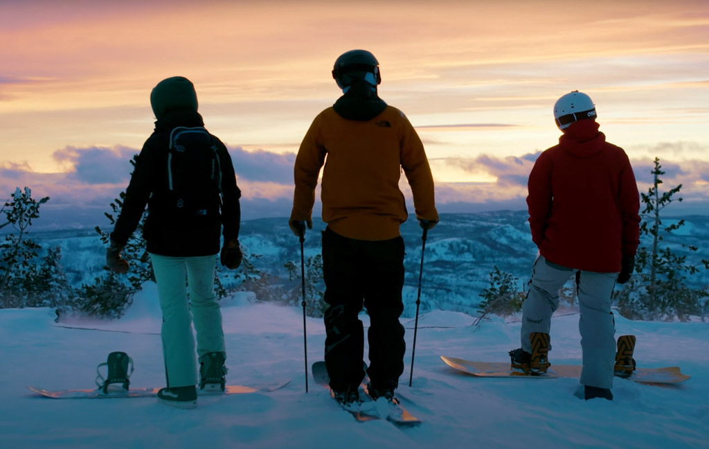 Skiers at sunset on snowy mountain ridge.