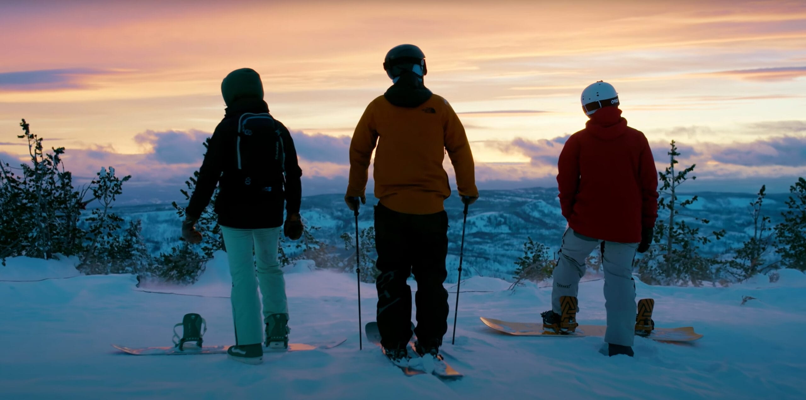 Three skiers watch sunset on snowy mountain.