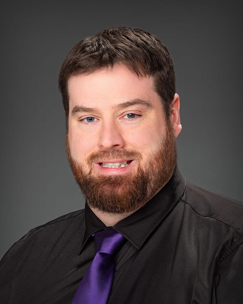 Man in black shirt and purple tie smiling