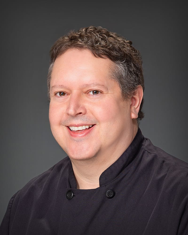 Smiling chef in black uniform on gray background