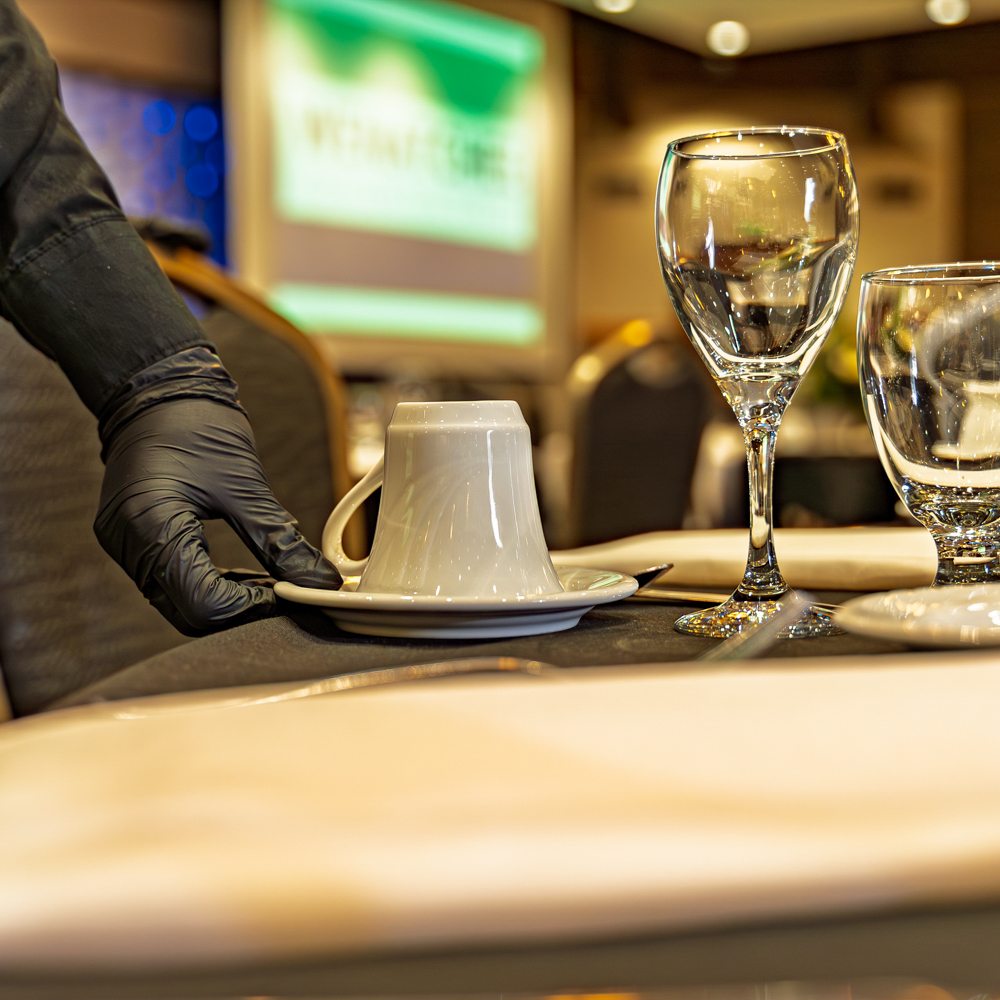 Gloved server sets table for event.