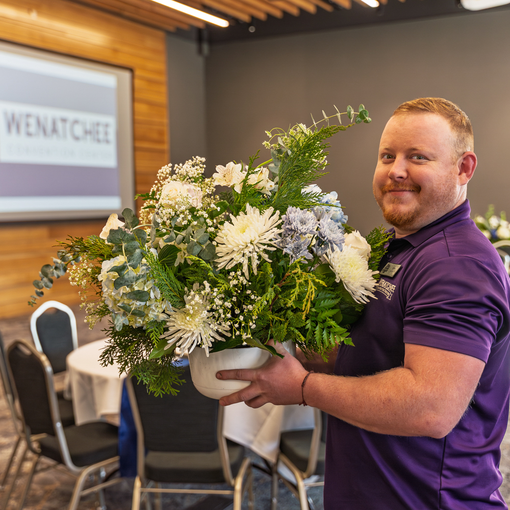 Man holding floral arrangement at convention center event.