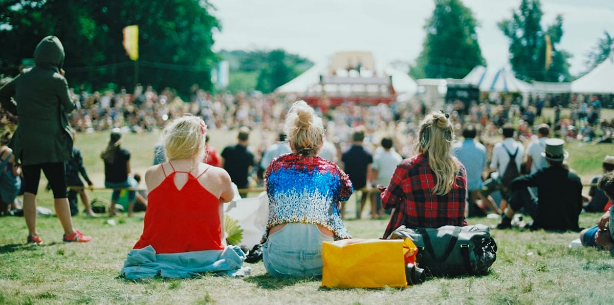 People enjoying outdoor festival with tents and crowd.