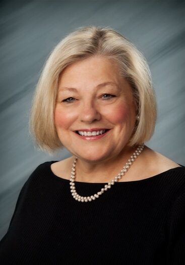 Smiling woman with short blonde hair and pearls.