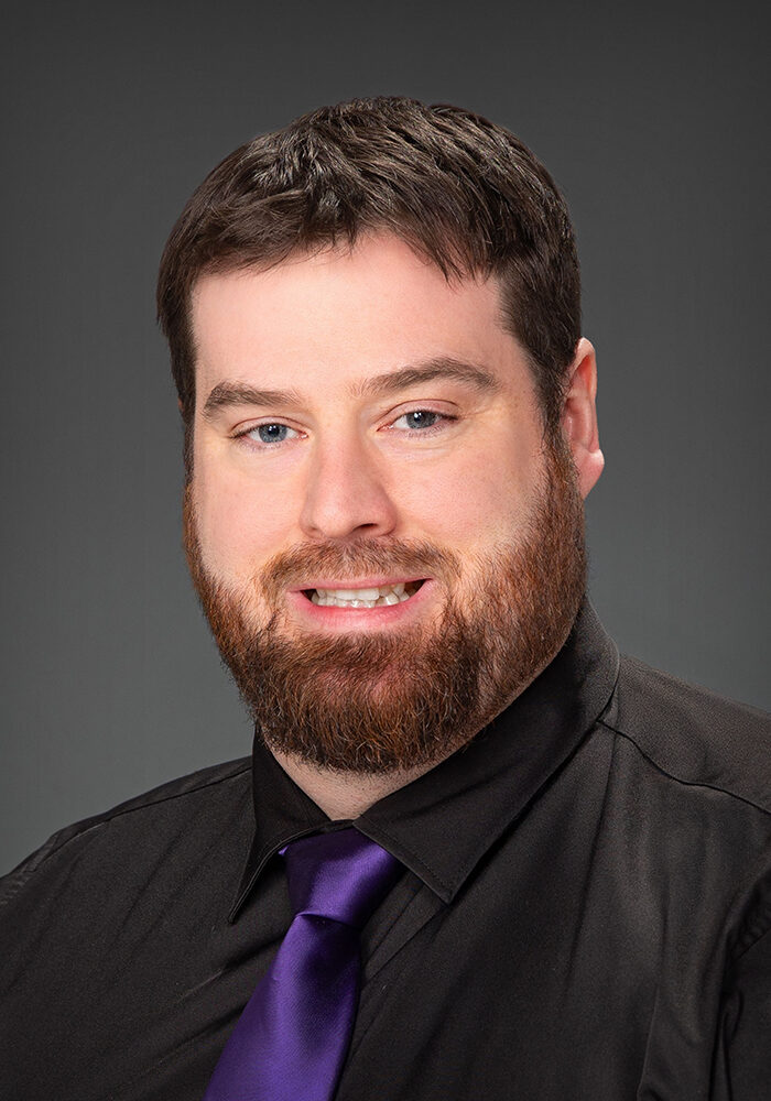 Man in black shirt and purple tie smiling